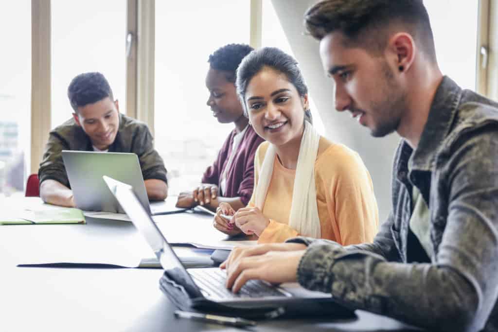 Young man using laptop with female student watching and smiling