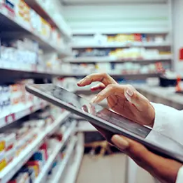 Pharmacist holding a tablet near shelves of medications