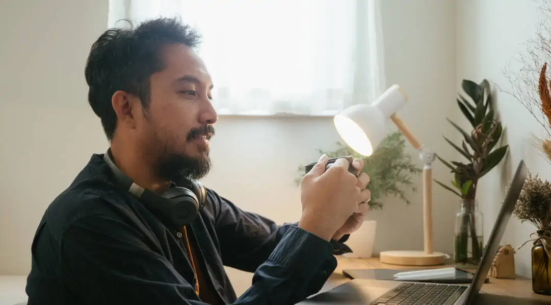 Man drinking coffee or tea looking at laptop