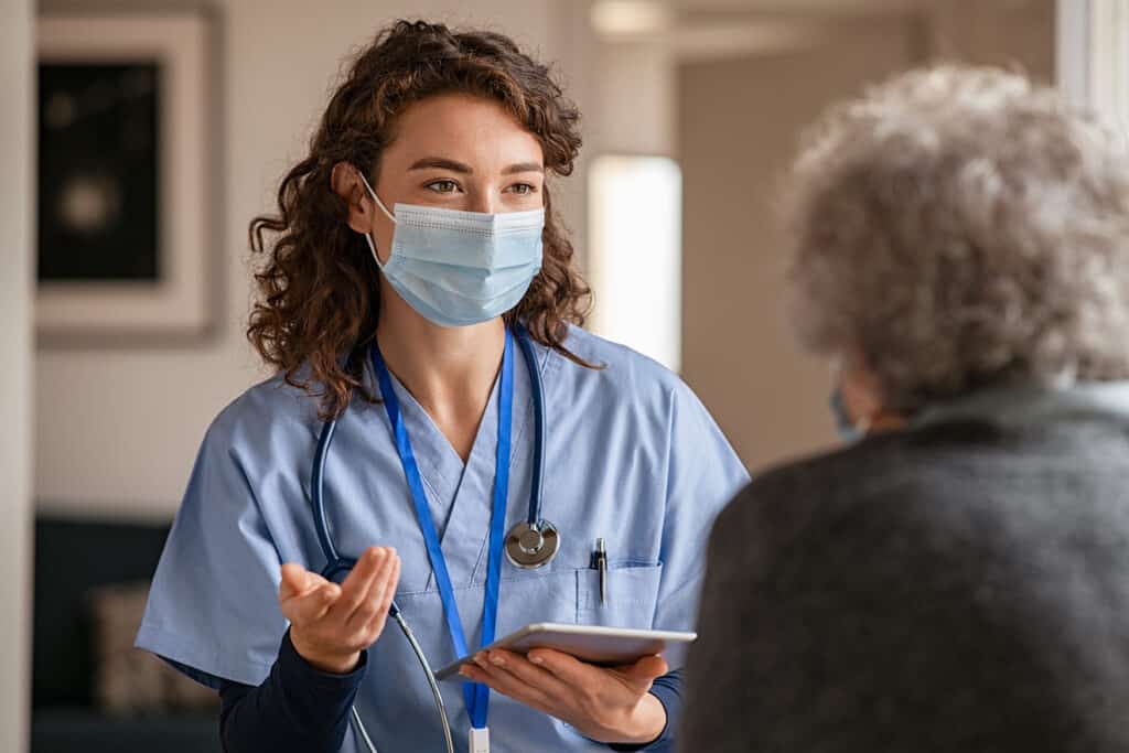 A healthcare worker wearing a mask speaks with a patient.