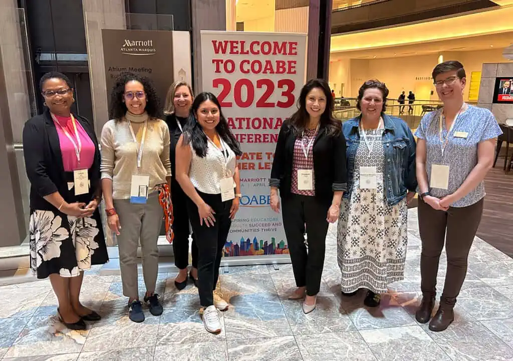 Six adults pose for group shot in front of COABE 2023 conference banner.