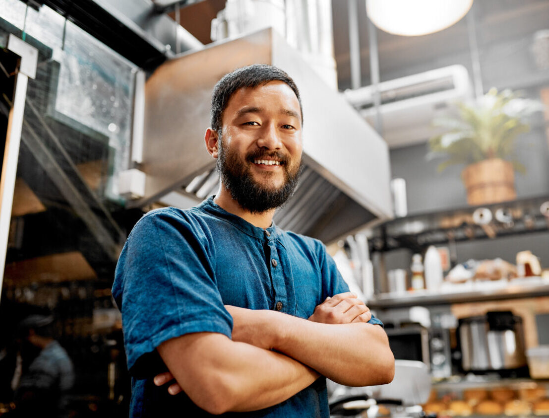 Portrait of a handsome young barista posing with his arms folded inside a cafe