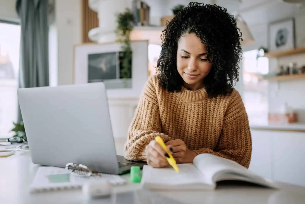 Woman highlighting book in front of laptop