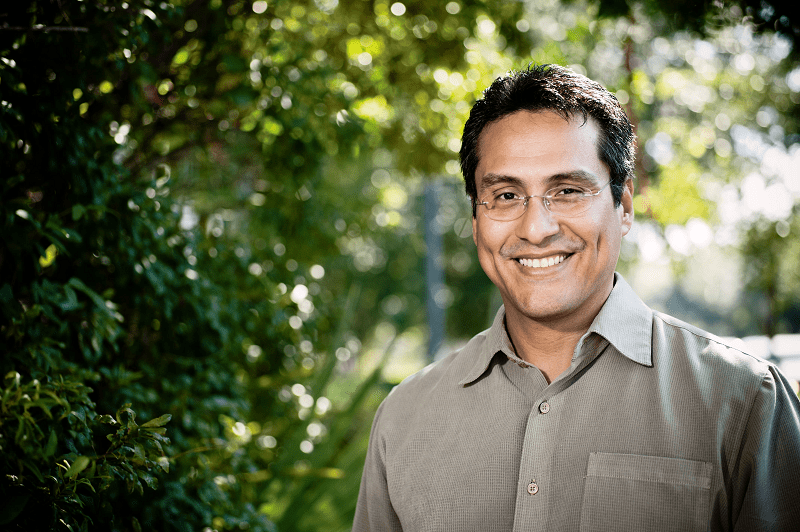 Man with glasses smiling next to a tree